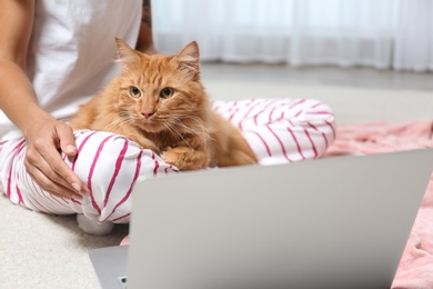 Woman with cute red cat and laptop at home, closeup view. Space for text
