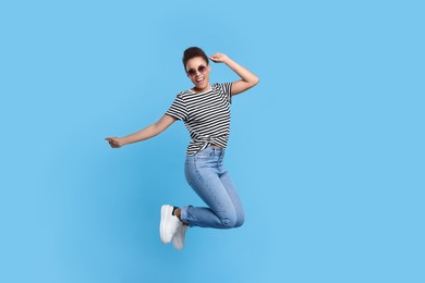 Photo of Happy young woman jumping while dancing on light blue background