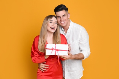 Photo of Lovely couple with gift on yellow background. Valentine's day celebration