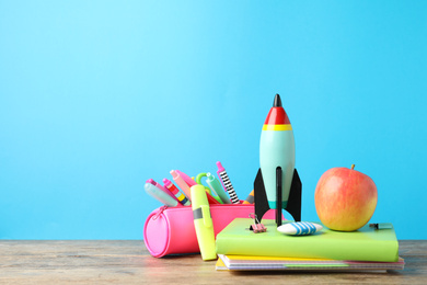 Photo of Bright toy rocket and school supplies on wooden table. Space for text