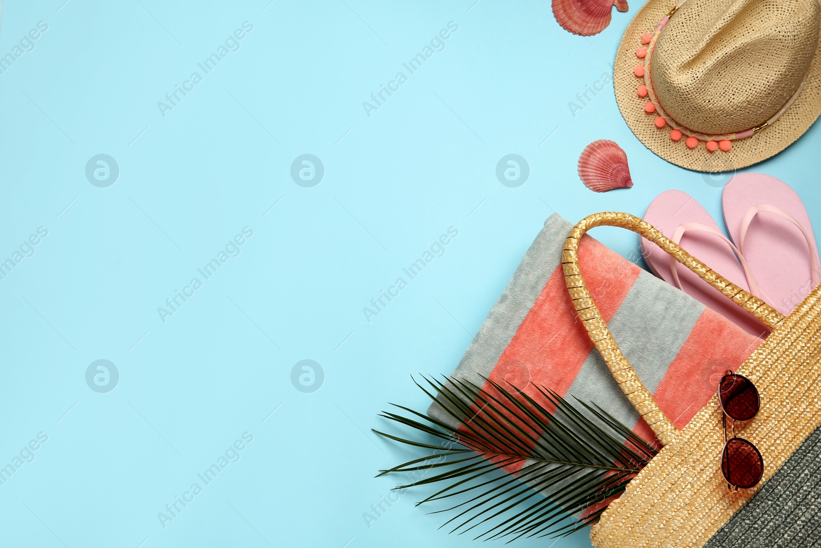 Photo of Beach bag with towel, flip flops , sunglasses and hat on light blue background, flat lay. Space for text