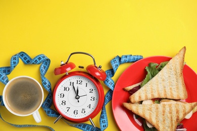 Photo of Flat lay composition with tasty sandwiches and alarm clock on yellow background, space for text. Nutrition regime