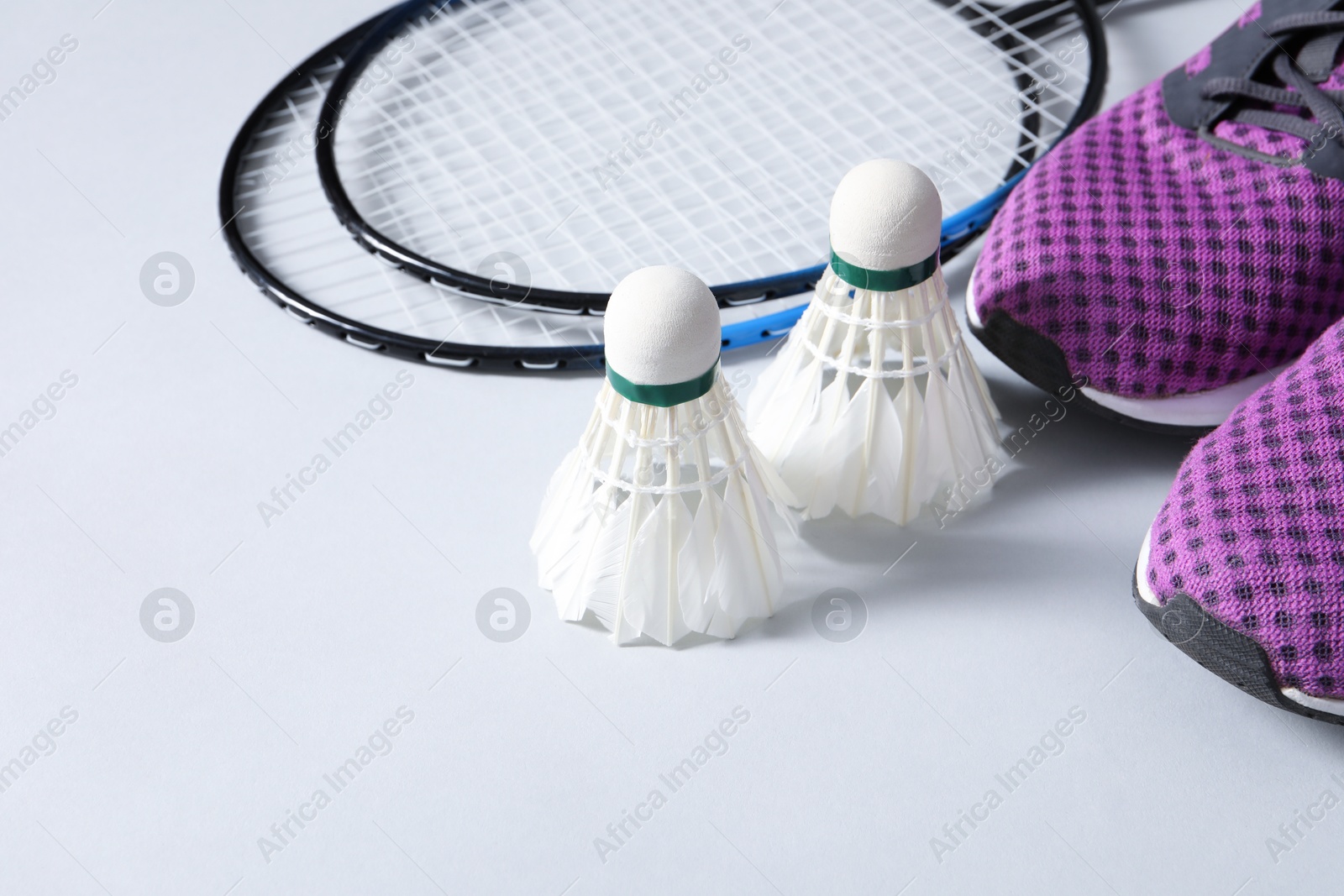 Photo of Feather badminton shuttlecocks, rackets and sneakers on gray background, space for text