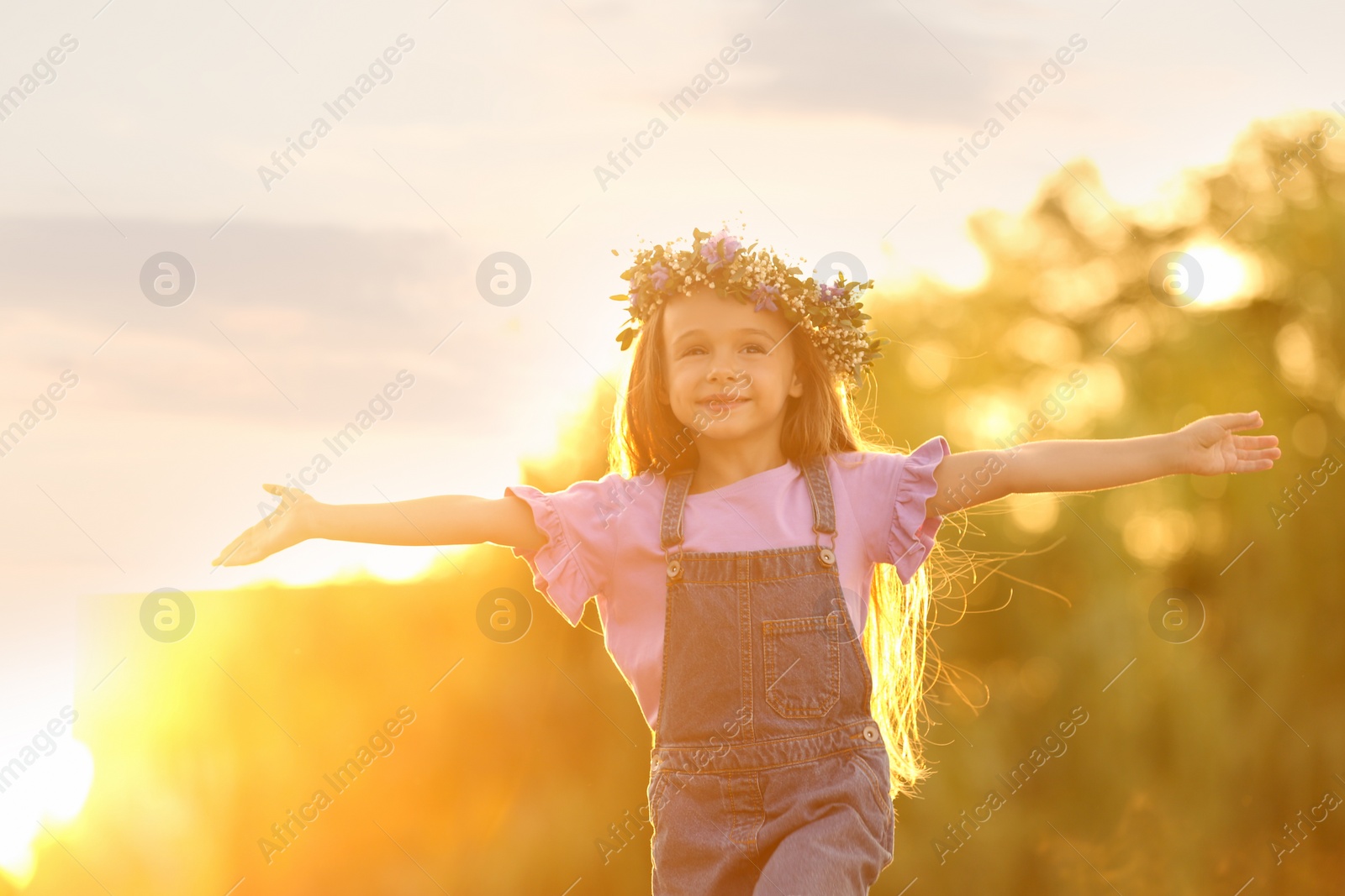 Photo of Cute little girl wearing flower wreath outdoors at sunset. Child spending time in nature
