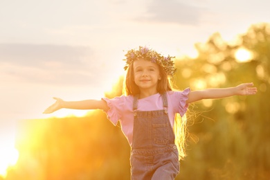 Cute little girl wearing flower wreath outdoors at sunset. Child spending time in nature