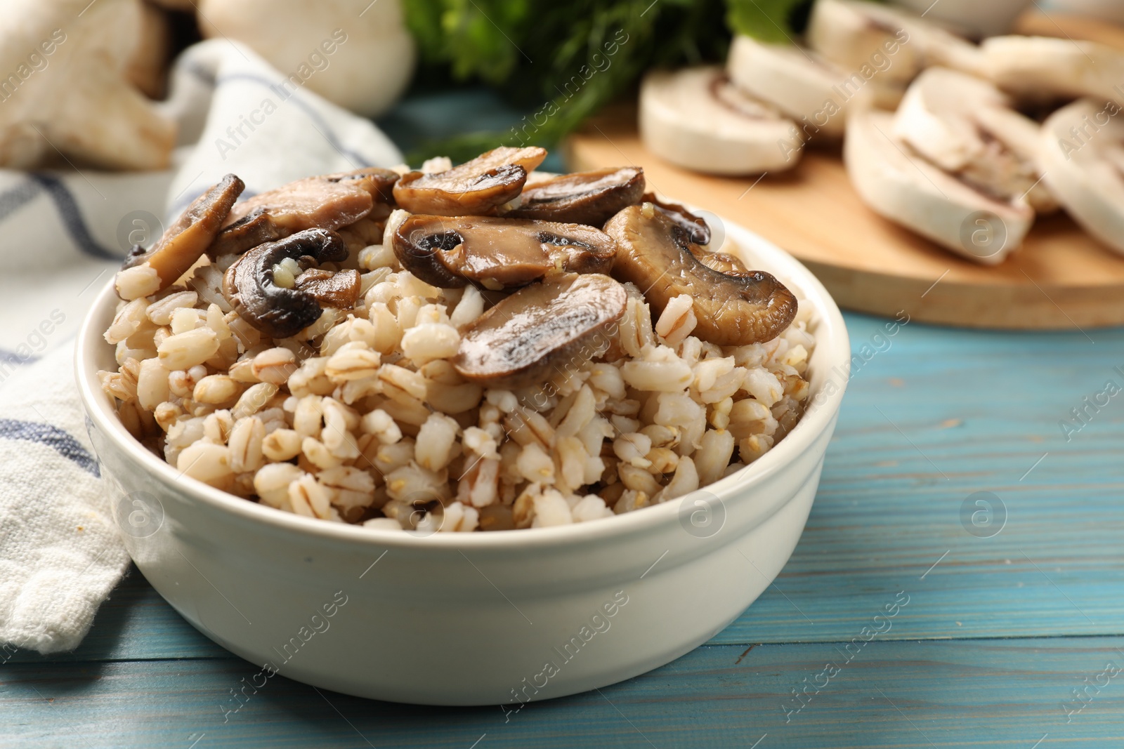 Photo of Delicious pearl barley with mushrooms in bowl on light blue wooden table, closeup