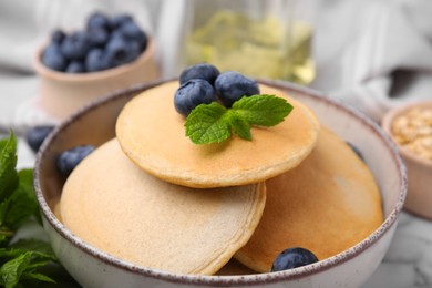 Bowl with tasty oatmeal pancakes, mint and blueberries on table, closeup