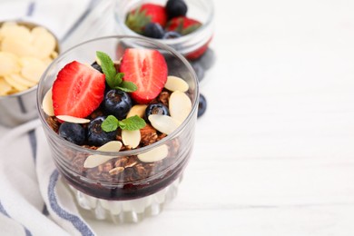 Photo of Tasty granola with berries, jam, yogurt and almond flakes in glass on white table, closeup. Space for text