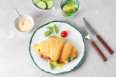 Tasty croissant sandwich with salami on light background