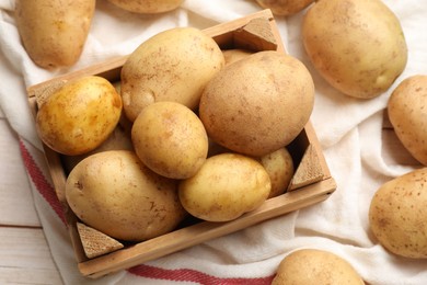 Photo of Raw fresh potatoes with crate on light wooden table, top view