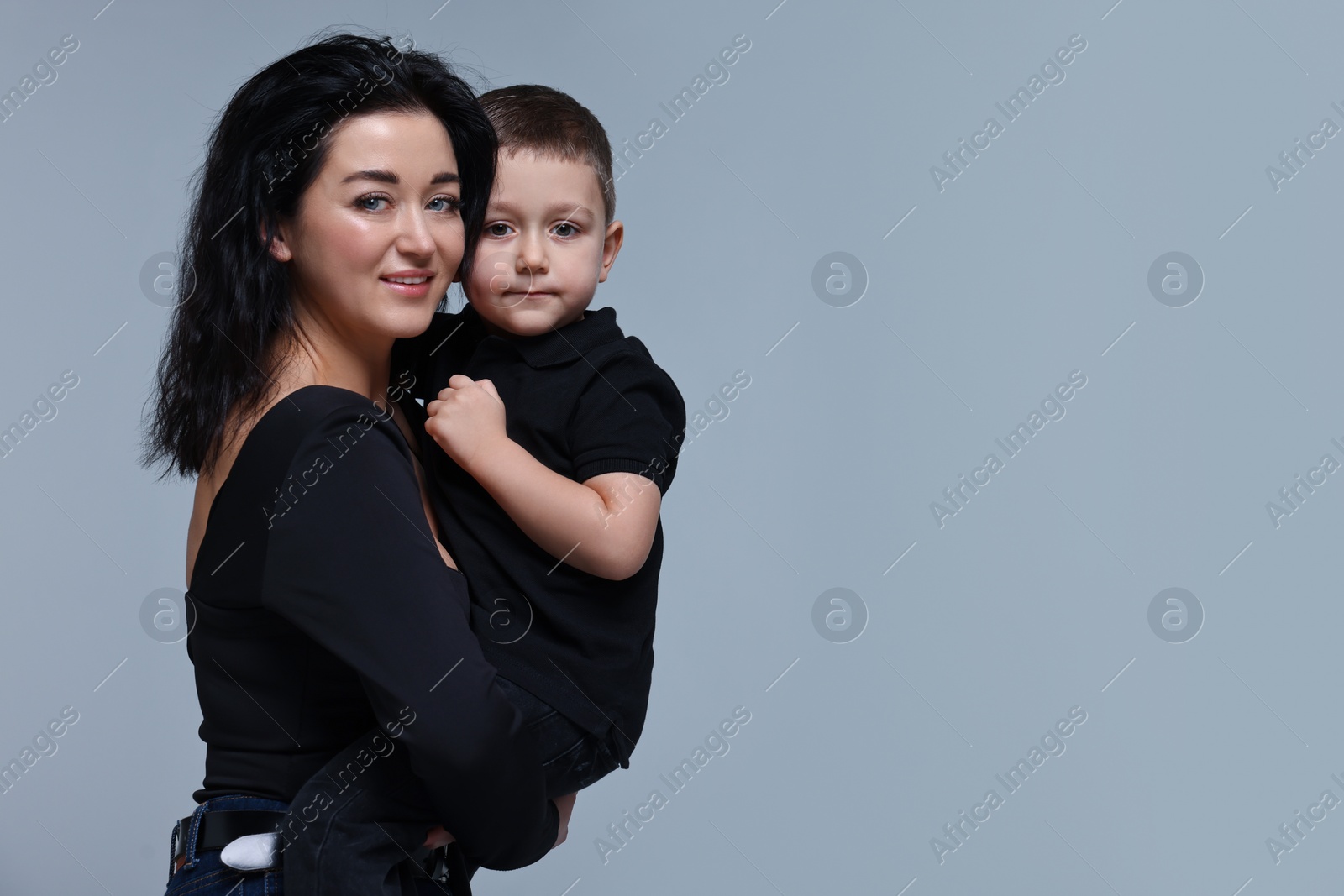 Photo of Beautiful mother hugging little son on grey background. Space for text