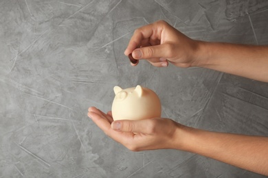 Photo of Woman putting coin into piggy bank on grey stone background, closeup view