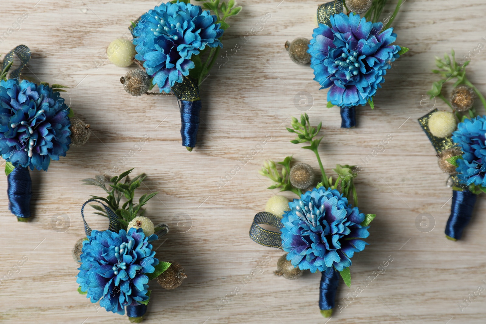 Photo of Stylish blue boutonnieres on white wooden table, flat lay