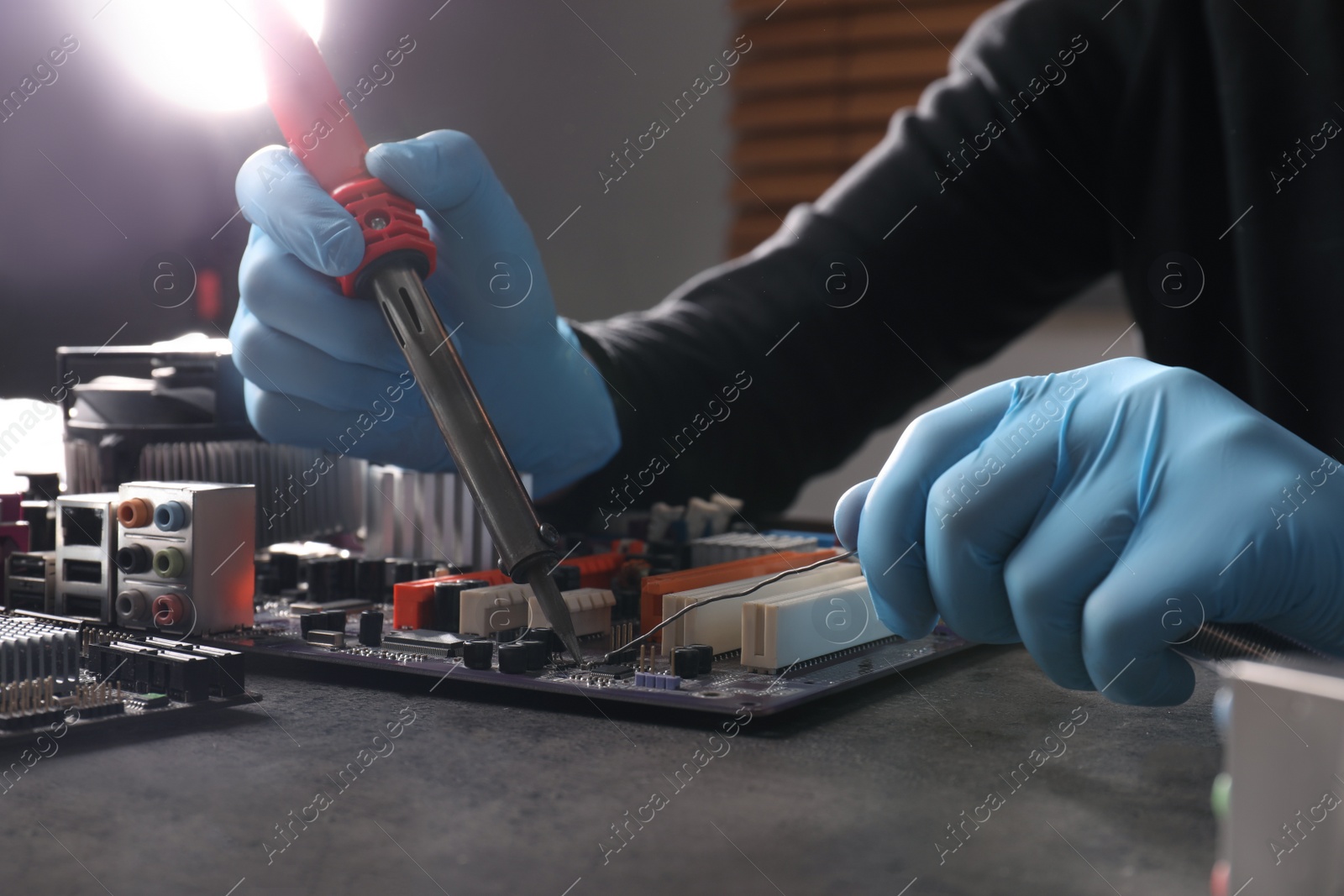 Photo of Technician repairing electronic circuit board with soldering iron at table, closeup