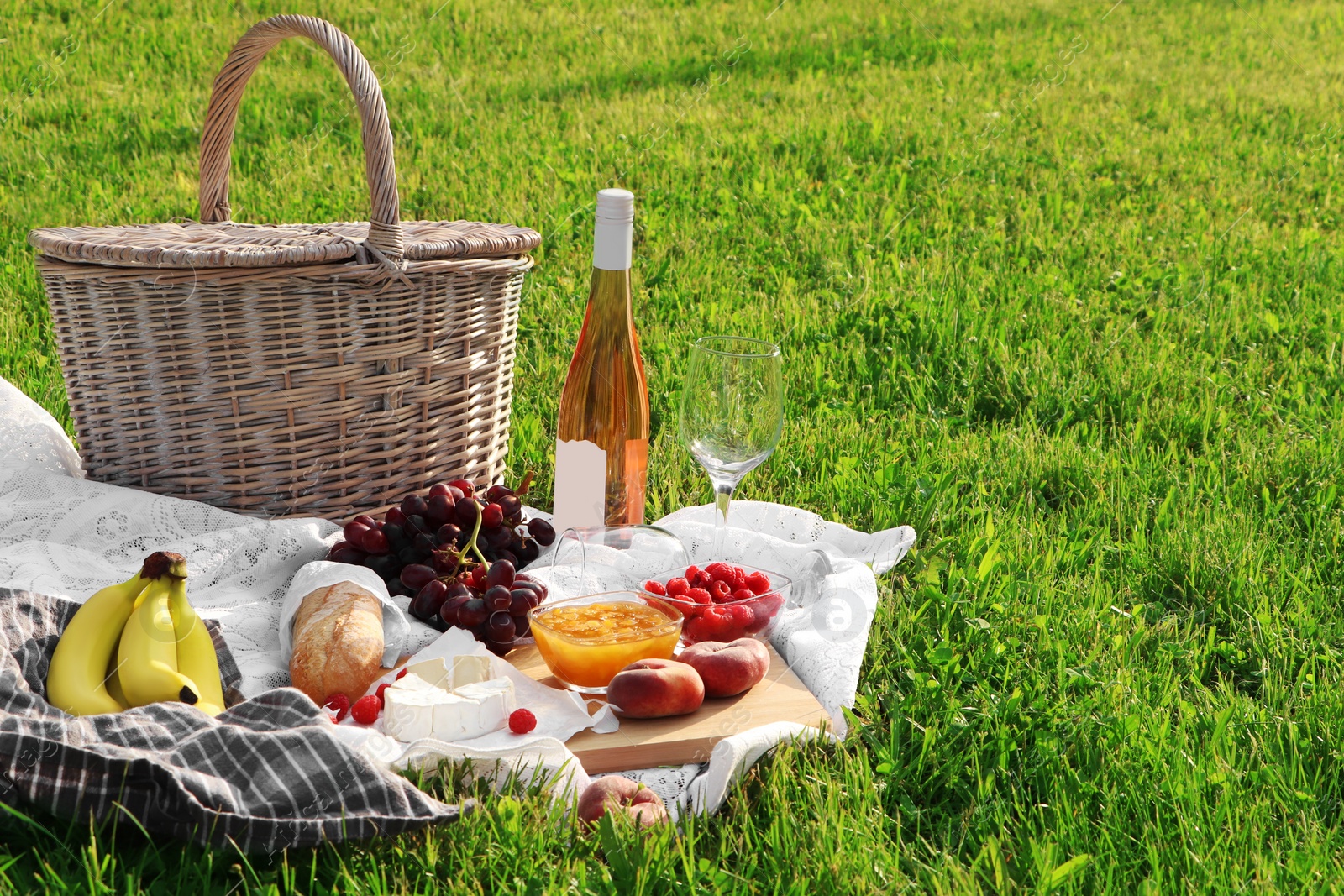 Photo of Picnic blanket with tasty food, basket and cider on green grass outdoors. Space for text