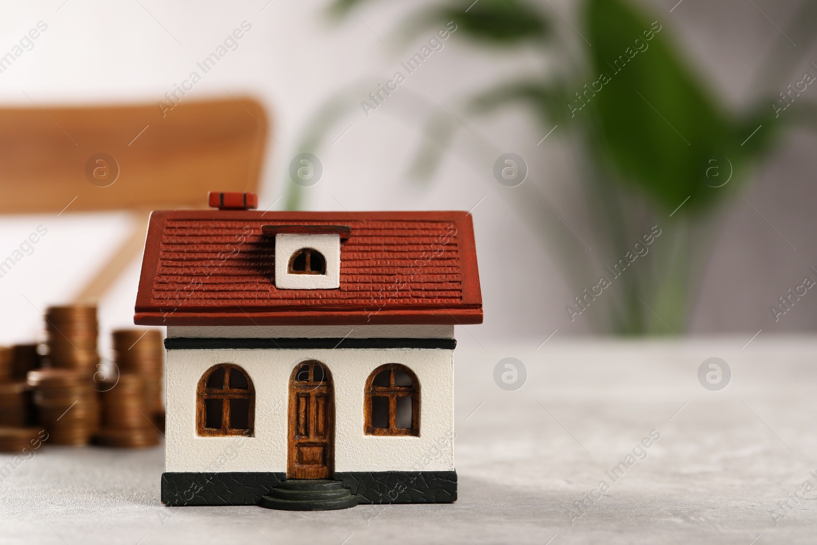 Photo of House model and stacked coins on grey table indoors, selective focus. Space for text