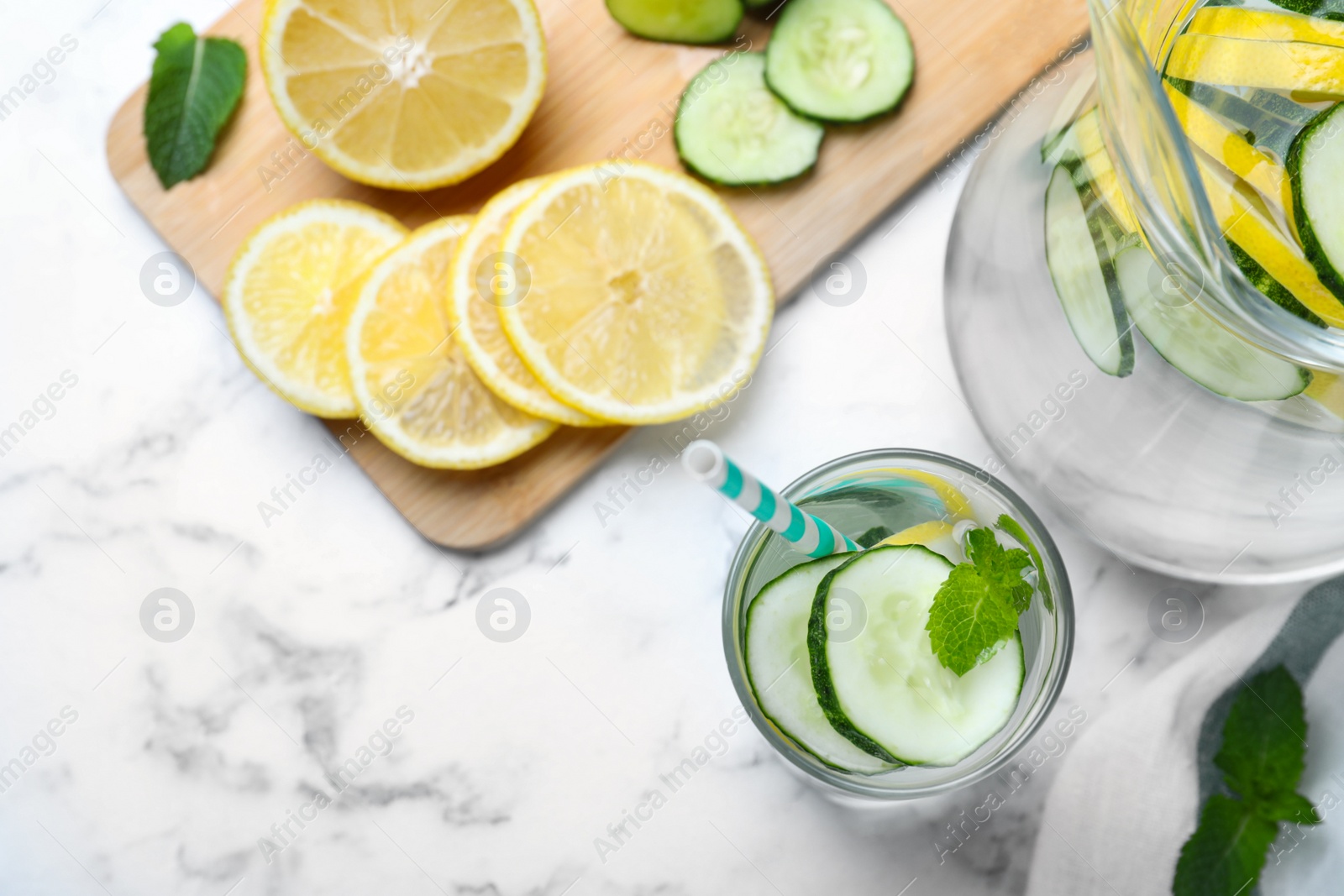 Photo of Refreshing water with cucumber, lemon and mint on white marble table, flat lay