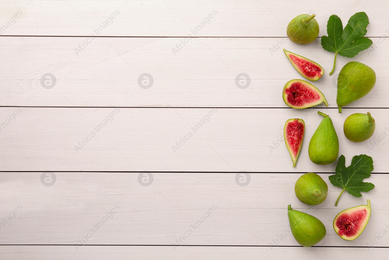 Photo of Cut and whole green figs with leaves on white wooden table, flat lay. Space for text