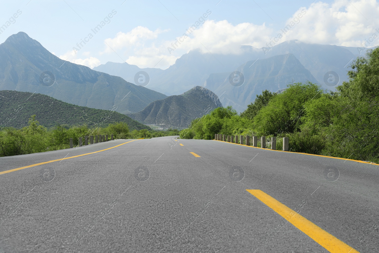 Photo of Picturesque view of big mountains and bushes near road under cloudy sky