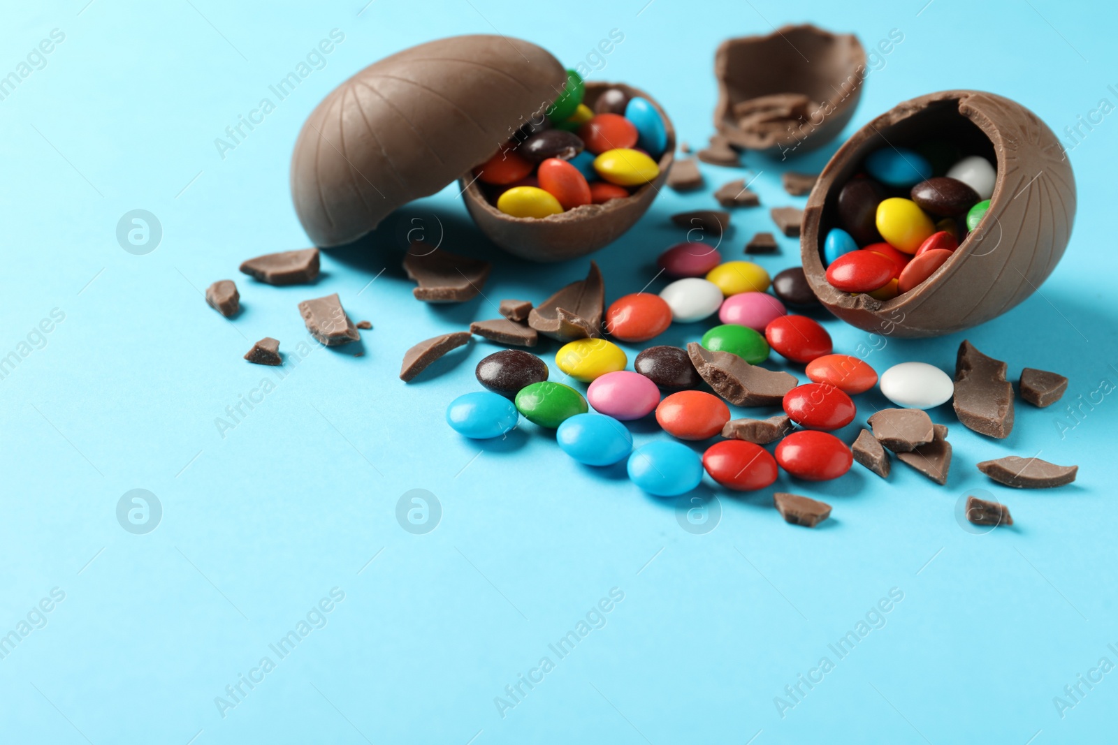 Photo of Broken chocolate eggs with candies on light blue background, space for text