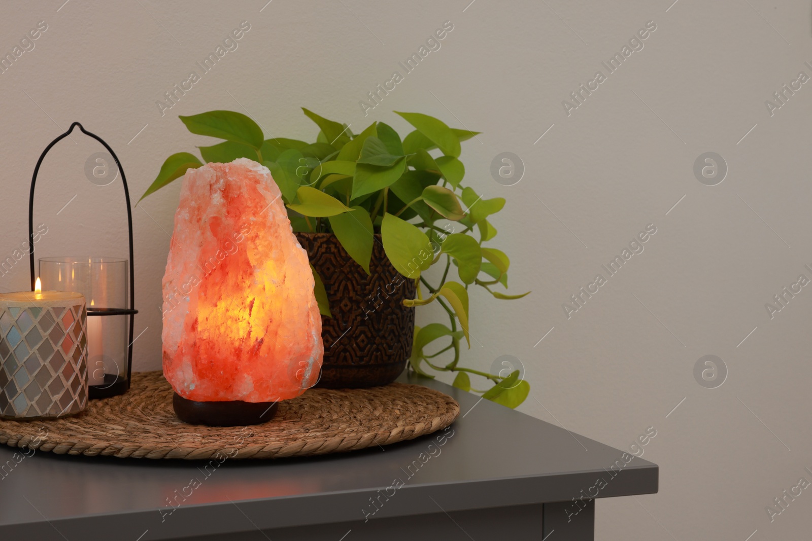 Photo of Himalayan salt lamp, houseplant and candles on grey table near light wall, space for text