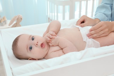 Mother changing baby's diaper on table at home