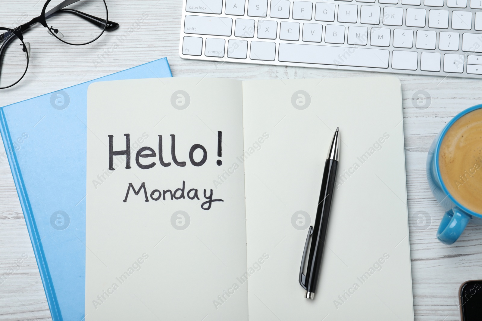 Photo of Message Hello Monday written in notebook, computer keyboard and cup of coffee on white wooden desk, flat lay