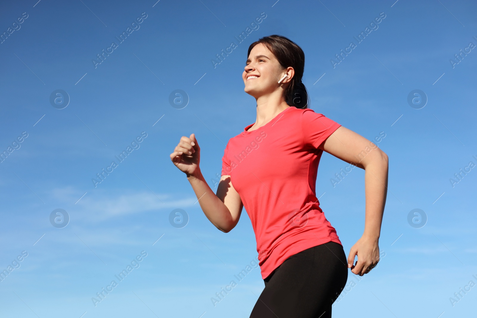 Photo of Young woman listening to music while running outdoors in morning, low angle view. Space for text