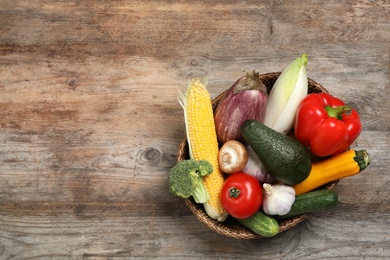 Photo of Wicker bowl with different fresh vegetables on wooden background, top view. Space for text