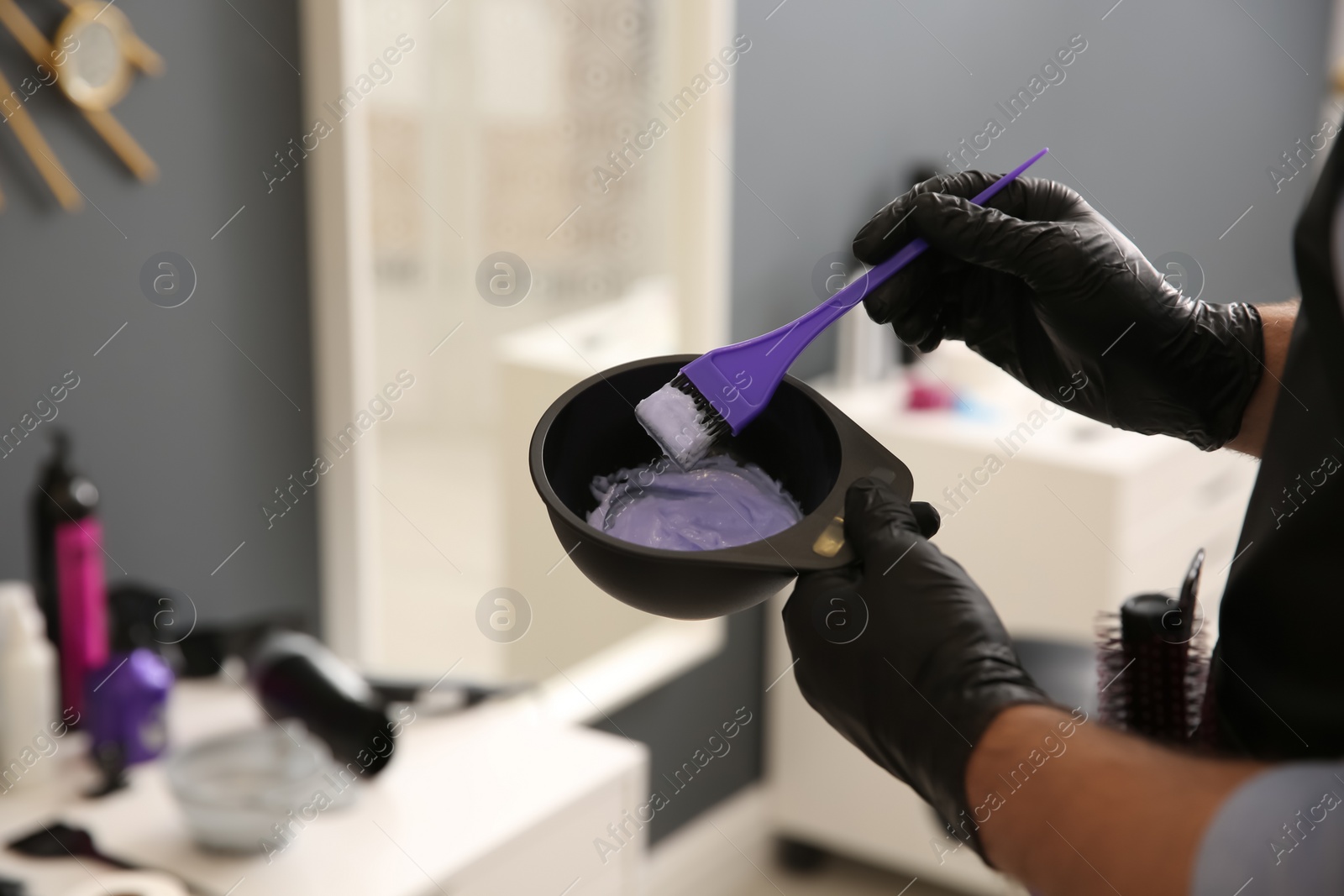 Photo of Professional hairdresser holding bowl with hair dye in beauty salon, closeup