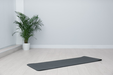 Unrolled black yoga mat on floor in room. Space for text