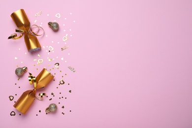 Photo of Open golden Christmas cracker and decorations with shiny confetti on pink background, flat lay. Space for text