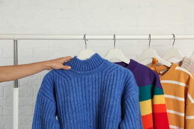 Photo of Woman choosing sweater on rack against brick wall