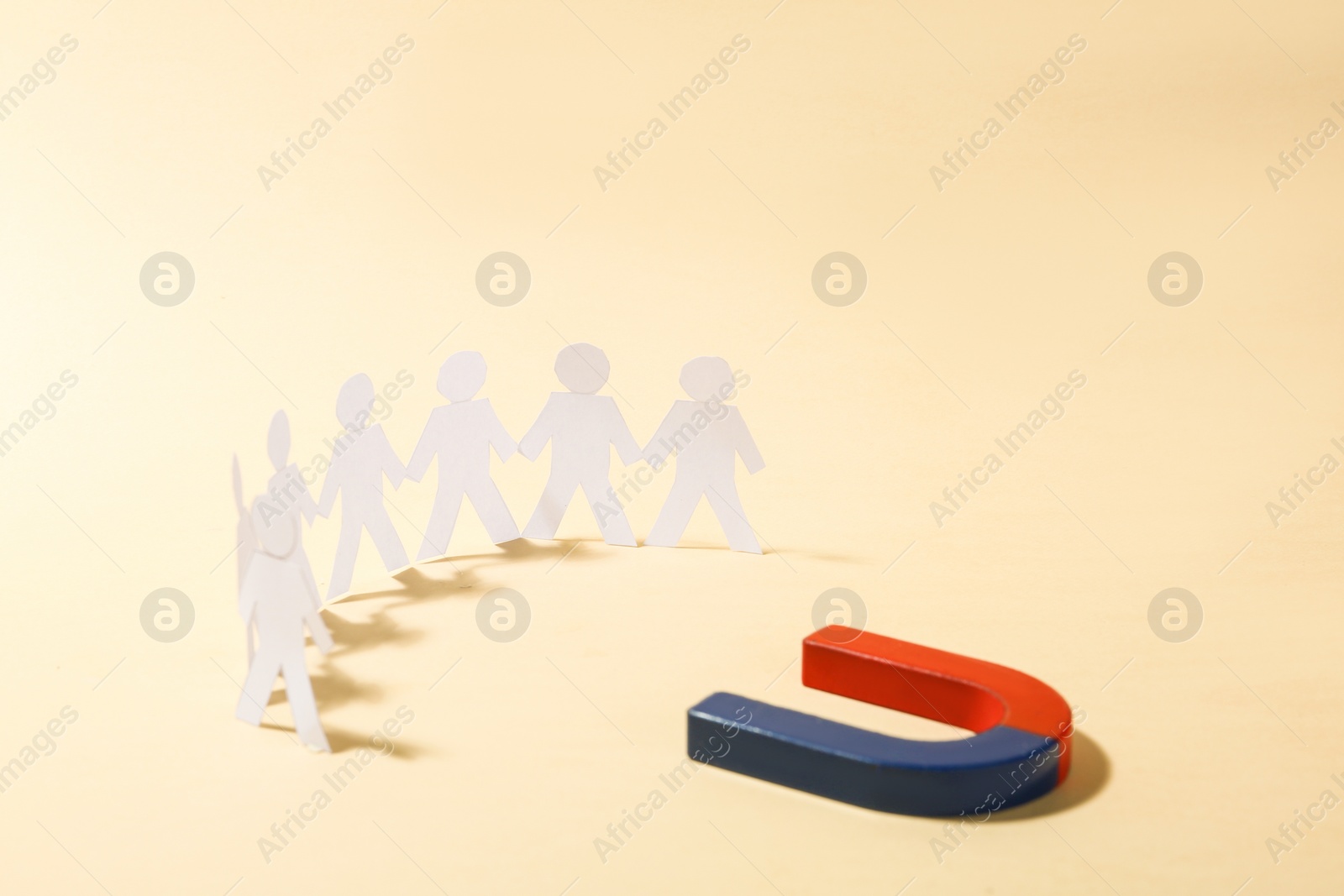 Photo of Magnet attracting paper people on beige background