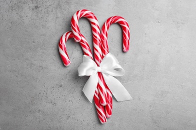 Sweet Christmas candy canes with white bow on grey background, top view