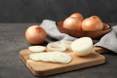 Photo of Wooden board with cut onion and bowl of bulbs on grey table