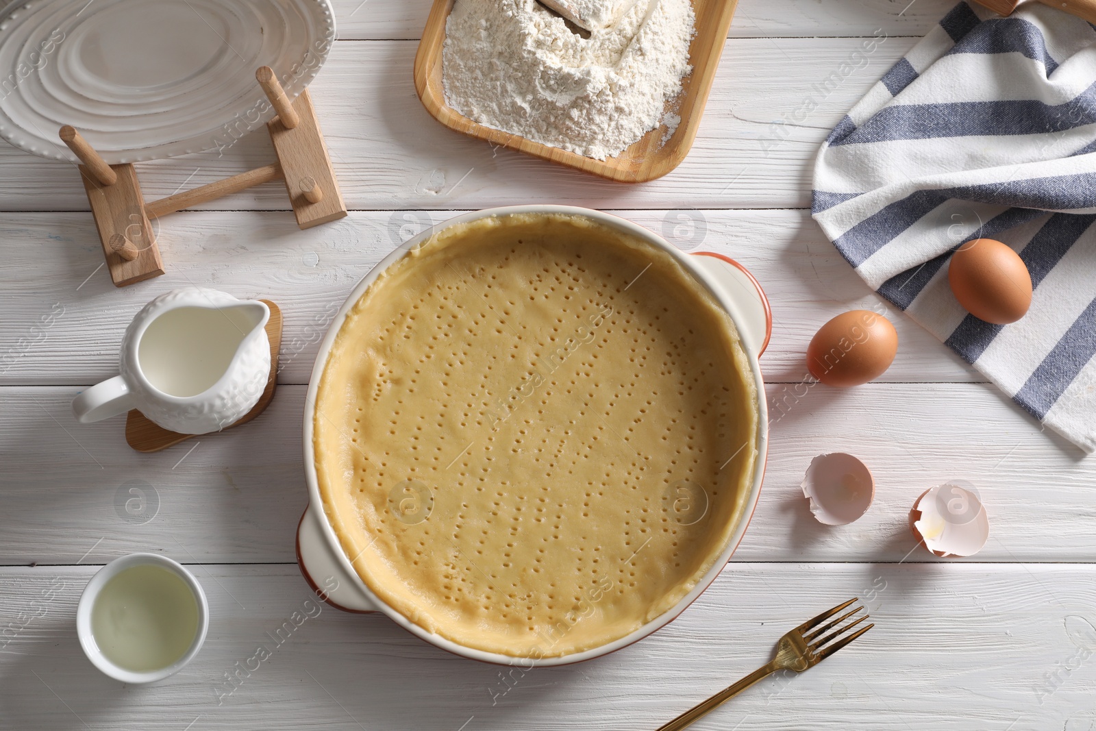 Photo of Pie tin with fresh dough and ingredients on white wooden table, flat lay. Making quiche