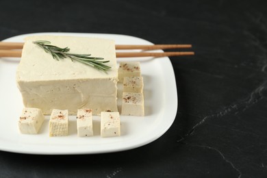 Photo of Pieces of delicious tofu with rosemary on black table. Soybean curd