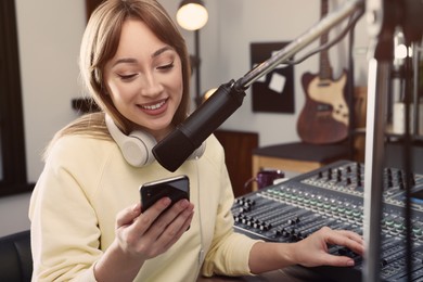 Photo of Woman with smartphone working as radio host in modern studio