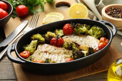 Photo of Tasty cod cooked with vegetables served on wooden table
