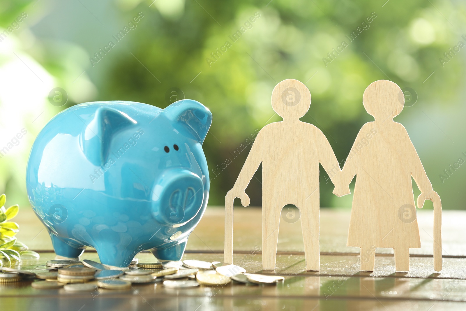 Photo of Pension savings. Figure of senior couple, piggy bank and coins on wooden table outdoors