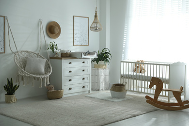 Chest of drawers with changing tray and pad near comfortable cradle in baby room. Interior design