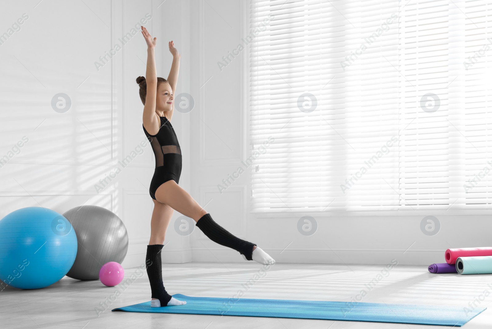 Photo of Cute little gymnast in leotard on mat indoors