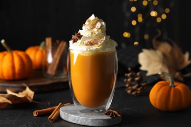 Photo of Glass of pumpkin spice latte with whipped cream and ingredients on black table
