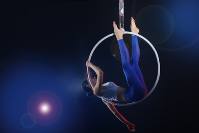 Photo of Young woman performing acrobatic element on aerial ring against dark background