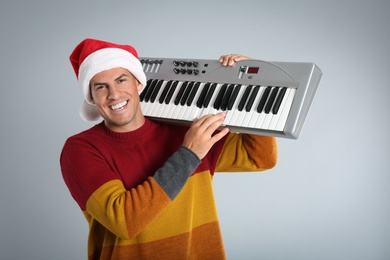 Photo of Man in Santa hat playing synthesizer on light grey background. Christmas music