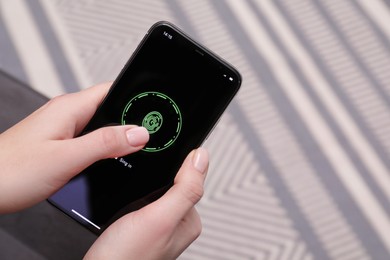 Woman unlocking smartphone with fingerprint scanner indoors, closeup
