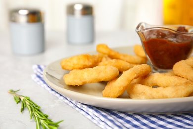Photo of Delicious crunchy fried onion rings and rosemary on light table, closeup