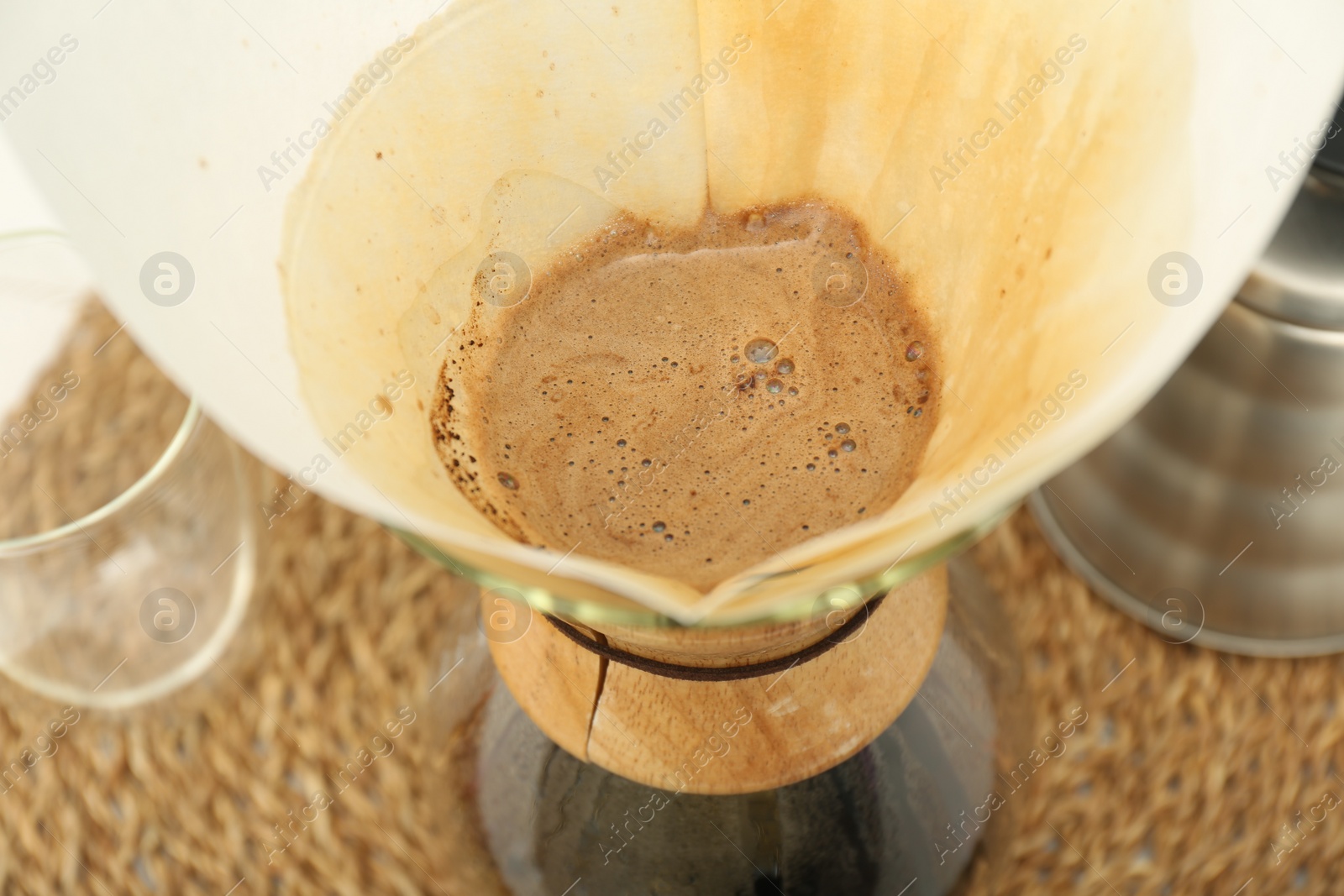 Photo of Paper filter with aromatic drip coffee in glass chemex coffeemaker on table, closeup