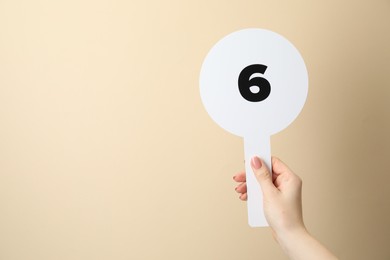 Photo of Woman holding auction paddle with number 6 on beige background, closeup. Space for text